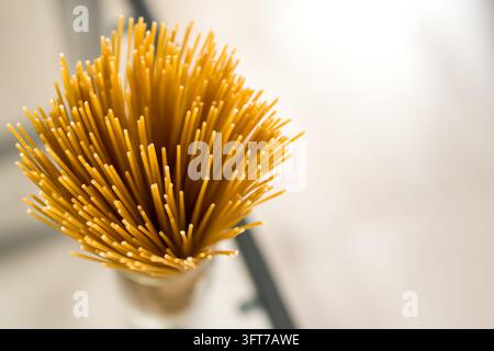 Makroaufnahme von oben eines dichten Bündels trockener, ungekochter gelber Spaghetti, die vertikal in einem Glasbehälter stehen. Stockfoto