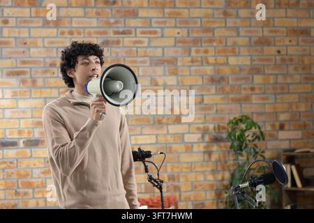 Afroamerikanischer Mann steht links im Studio und spricht in ein Megaphon in einem beigen Pullover, Kopierraum Stockfoto