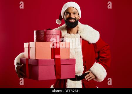 Ein bärtiger Mann in einem Weihnachtsmannkostüm lächelt und hält helle Geschenke vor einem roten Hintergrund. Stockfoto