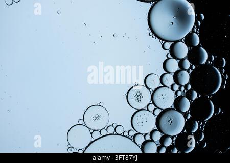Abstrakte Ansicht von runden Öltropfen, die auf der Oberfläche von flüssigem Wasser schweben und geometrische Muster aus Kugeln und Kreisen erzeugen Stockfoto
