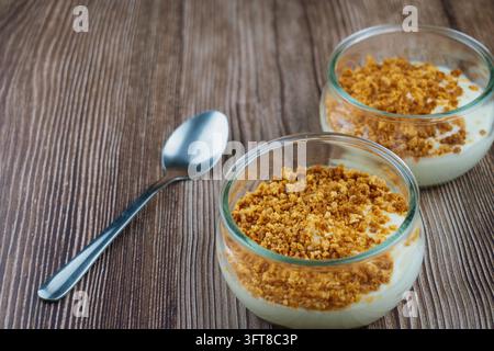 Zwei Gläser gefüllt mit cremigem Ricotta-Dessert und knusprigem Kekskrümel-Topping, serviert auf dunklem Holzgrund für süße Lebensmittel-Fotografie Stockfoto