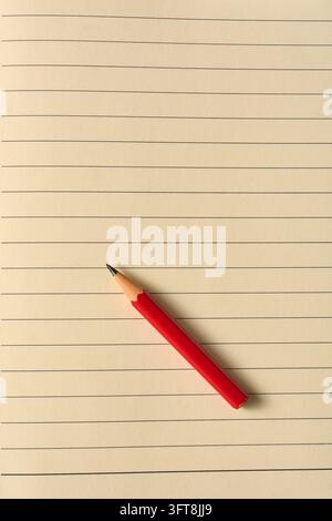 kurzer roter Stift auf liniertem Notizbuchpapier-Hintergrund, von oben aufgenommen, Bildungsbegriff mit Kopierplatz Stockfoto