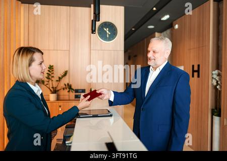 Erfahrener erwachsener Geschäftsmann, der sich an der Hotelrezeption anmeldet Stockfoto
