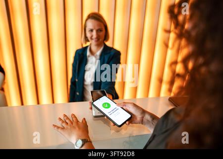 Frau, die an der Hotelrezeption kontaktlos mit Smartphone bezahlt Stockfoto