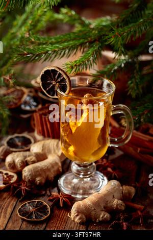 Ingwertee mit Gewürzen und Tannenzweigen. Heißes Wintergetränk mit Gewürzen und getrockneten Zitrusfrüchten auf einem alten Holztisch. Stockfoto