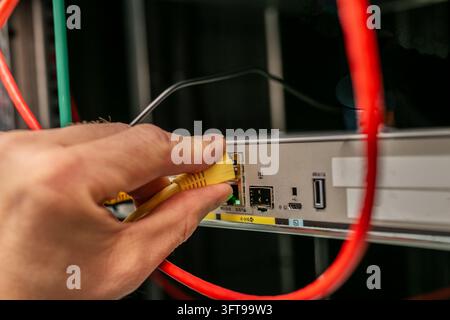 Nahaufnahme einer Person, die ein Ethernet-Patchkabel in einen Netzwerkanschluss an einem Switch oder Patchpanel innerhalb eines Serverracks steckt. Stockfoto
