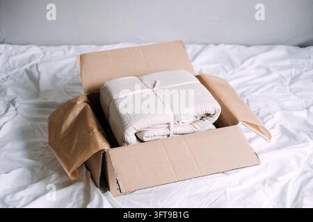 Gefaltetes, gekräuseltes Baumwollgazen-Bettwäsche in einem mit Kraftpapier ausgekleideten Paket, da immer mehr Haushalte Heimtextilien online kaufen Stockfoto
