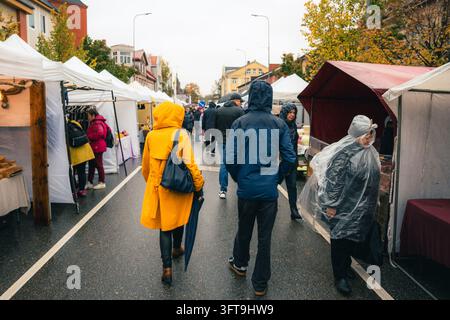 VALMIERA, LETTLAND – 10. OKTOBER 2026: Einkäufer in Regenmänteln und mit Regenschirmen auf einem Straßenmarkt im Freien an einem regnerischen Herbsttag Stockfoto