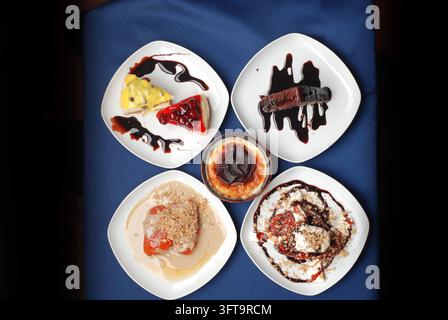 Oberblick auf verschiedene köstliche Desserts, die auf weißen Tellern über einer blauen Tischdecke serviert werden Stockfoto