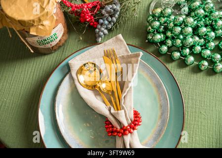 Elegante Feiertagstischgedeck mit weißem Teller und goldenem Besteck. Festliche Platzierung zur Feier des Heiligabends. Stockfoto
