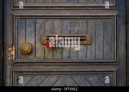 Alte Holztür mit Briefschlitz. Vintage-Tür mit Messing-Briefschlitz, der gefaltetes gedrucktes Papier hält, dekorative runde Beschläge. Verwitterte blaue Holz- Stockfoto
