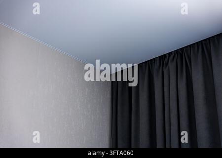 Minimalistische Innerecke zeigt eine strukturierte hellgraue Wand, bodentiefe schwarze Vorhänge und eine blau getönte Decke mit Kronenleiste. Stockfoto