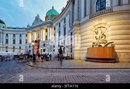 Fiaker-Kutschen und Fußgänger passieren den kaiserlichen Michaelertrakt und seinen Brunnen, während Anfang November ein Weihnachtsbaum aufgestellt wird, Österreich. Stockfoto