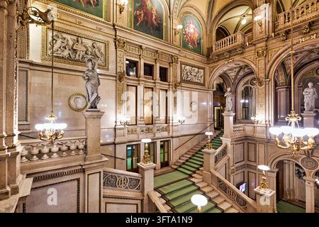 Marmortreppe mit grünem Teppich, allegorischen Statuen, vergoldeten Kronleuchtern und Fresken in der Wiener Staatsoper, einem Opernhaus aus dem 19. Jahrhundert Stockfoto