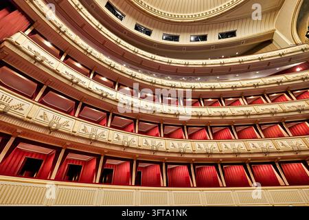 Niedrigwinklige Ansicht des leeren hufeisenförmigen Saals der Wiener Staatsoper in Wien, mit rot gepolsterten Logen und cremefarbenen und goldenen Balkonfronten. Stockfoto