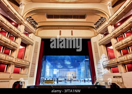 Techniker bauen die Bühne auf, gesehen aus dem leeren Auditorium, eingerahmt von roten Vorhängen und Reihen vergoldeter Logen, im Wiener Opernhaus Stockfoto
