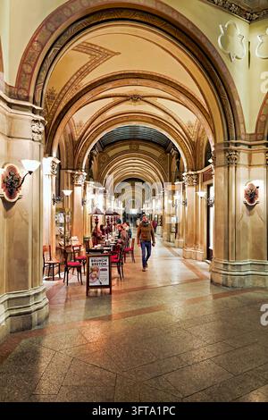 Café-Tische säumen die bemalte gewölbte Einkaufspassage des Palais Ferstel auf der Freyung in der Inneren Stadt Wiens, Österreich, während Fußgänger hindurchgehen. Stockfoto