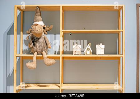 Ein niedliches Rentier-Ornament auf einem Holzregal neben Keramikhäusern; eine Weihnachtsstimmung. Stockfoto