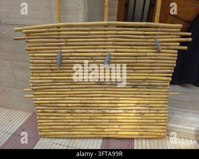 Handgefertigter Sichtschutz und Zaunpaneel, der aus getrockneten Stängeln der Riesenschilf-Pflanze Arundo donax hergestellt wird. Horizontale gelbe Schilfstängel sind vertikal gebunden Stockfoto
