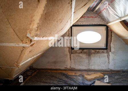 Ein kleines ovales Dachfenster sitzt in einer unbeendeten Dachbodenwand zwischen sichtbarer Dämmung und freiliegendem Mauerwerk, Altbaurenovation, Stuttgart, Baden-Wuert Stockfoto