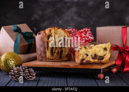 Traditioneller italienischer Weihnachts-Schokoladenstück-Panettone, Chocottone, auf einem Holzbrett geschnitten, mit verpackten Geschenkkisten, Tannenzapfen und einem goldenen Kugelornament Stockfoto