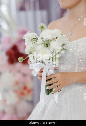 Braut in funkelndem Kleid hält einen weißen Ranunkulus-Hochzeitsstrauß Stockfoto