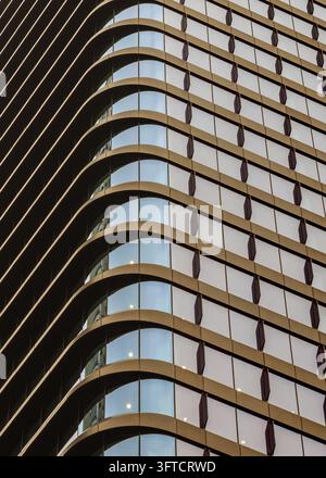 Abstrakte Vollbildansicht einer modernen Hochhausfassade mit gebogenen bronzenen horizontalen Bändern und einem Glasfenster-Rastermuster. Stockfoto