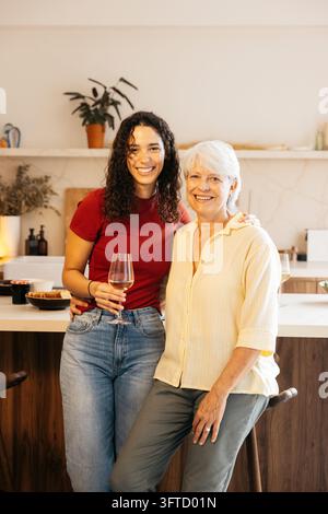 Mutter und Tochter lächeln, stehen zusammen mit Weingläsern in einer modernen Küche Stockfoto