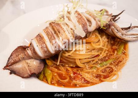 Köstliches italienisches Pastagericht mit einem ganzen gegrillten Tintenfisch über Spaghetti in einer reichhaltigen Tomatensoße. Stockfoto
