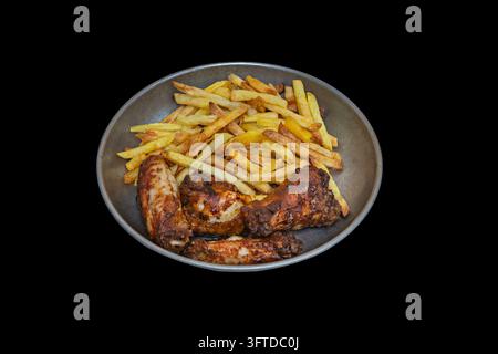 Glasiierte gebratene Hühnerflügel und -schenkel mit goldenen handgeschnittenen Pommes auf einem verwitterten Metallteller, isoliert vor einem soliden schwarzen Hintergrund Stockfoto
