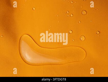 Makroaufnahme von Regentropfen auf lebhaftem orangefarbenem hydrophobem Stoff Stockfoto