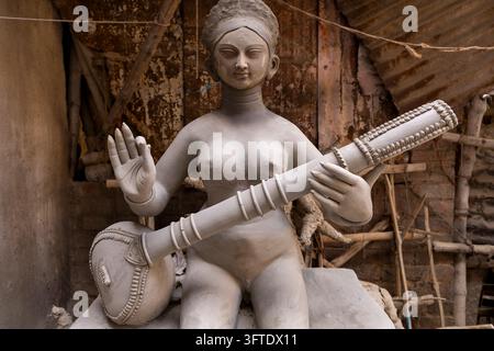 Graue Ton-Göttinnenfigur mit erhobener Hand und einem Saiteninstrument vor einer Ziegelmauer im Bezirk Kumartuli, Westbengalen, Kalkutta, Indien Stockfoto