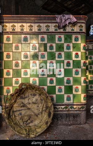 Dekorative Keramikfliesen mit roten Blumenmotiven säumen eine alte überdachte Halle mit einem leeren Korb auf dem Blumenmarkt, West Bengal, Kalkutta, Indien Stockfoto