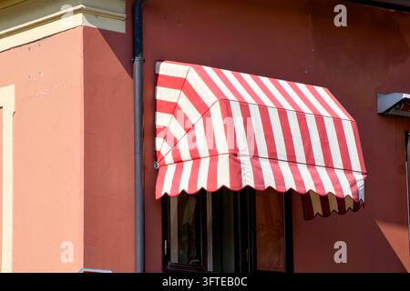 ein klassisches rot-weiß gestreiftes Vordach, das sich elegant über ein Fenster eines charmanten Gebäudes legt. Stockfoto