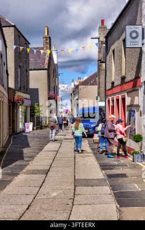 Fußgänger gehen durch eine enge Innenstadtstraße, die mit bunten Fähnchen geschmückt ist. Stockfoto