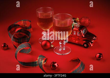 Festliches Stillleben mit Whiskeygläsern, rotem Spielzeugtruck und Geschenken, umgeben von roten Kugeln und Schottenband. Symbolische Feiersetting. Stockfoto
