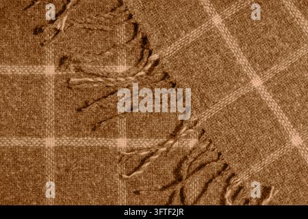 Orange karierte Decke mit dekorativem Fransenbesatz und gewebter Textur, die einen warmen textilen Hintergrund für Herbst-, Wintermode, Innenräume und gemütliches Design schafft Stockfoto