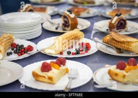 Eine verlockende Auswahl an frisch zubereiteten Waffeln, gerollten Waffelpuffer und verschiedenen Kuchen, die auf weißen Tellern an einem Desserttisch serviert werden. Stockfoto