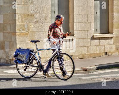 Mann geht neben seinem Fahrrad über eine Innenstadtstraße, während er auf sein Smartphone schaut - Tours, Indre-et-Loire (37), Frankreich. Stockfoto