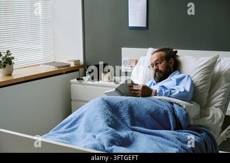 Mittelalter Mann liest Buch im Krankenhausbett zur Genesung Stockfoto