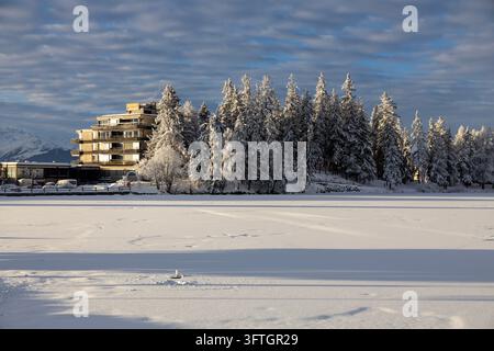 Hotelgebäude zwischen gefrorenen Tannen neben einem schneebedeckten gefrorenen See im Winter, Schweiz Stockfoto