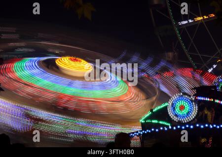 Farbenfroher sich drehender Jahrmarkt-Ritt bei Nacht mit lebendigen Lichtspuren und Bewegungsunschärfe Stockfoto