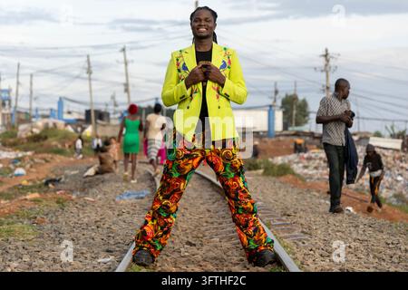 David Avido Modedesigner in einem limettengrünen Blazer und einer Hose mit Wirbelmuster, der auf einer Eisenbahnlinie sitzt, Nairobi County, Nairobi, Kenia Stockfoto