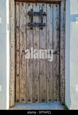 Eine antike verwitterte Holztür mit vertikalen, abgenutzten Holzplanken, runden Eisennieten und einem kleinen vergitterten Fensterrost. Die Tür ist Stockfoto