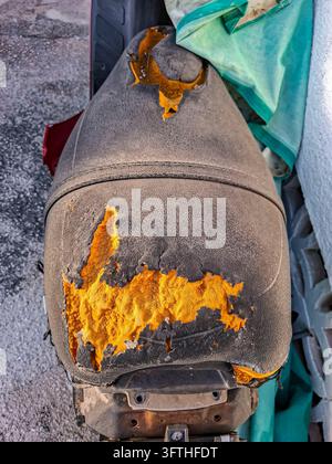 Hochwinklige Nahaufnahme eines alten, verwitterten Scooter-Sitzes mit stark zerrissenem und rissigem schwarzem Vinylbezug, der den abgenutzten gelben Innenfoam freilegt Stockfoto