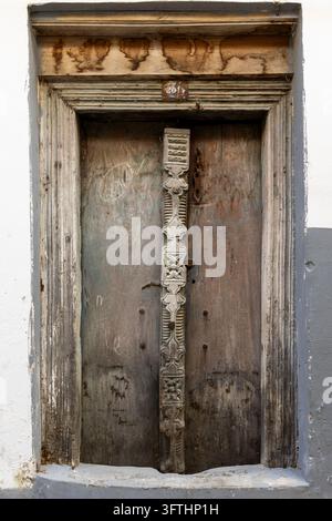 Verwitterte Holztür mit geschnitztem Mittelpfosten und altem Türsturz aus Holz in einer weiß getünchten und grau gestrichenen Wand, Stone Town, Tansania Stockfoto