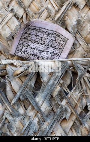 Altes abgenutztes Heft mit arabischer Schrift, das in eine verwitterte gewebte Palmenblattwand mit ausgefransten grauen und beigen Streifen gesteckt ist, Matemwe, Tansania Stockfoto