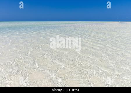 Kristallklares flaches Wasser, das bei Ebbe über weißen Sand in einer ruhigen tropischen Lagune unter einem tiefblauen Himmel schwappt, Jambiani, Tansania Stockfoto