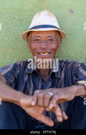 Älterer Mann lächelt, während er einen Strohhut trägt, vor einer grünen Wand, Vakinankaratra, Antsirabe, Madagaskar Stockfoto