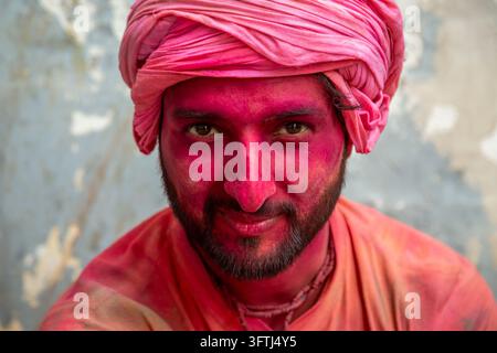 Porträt eines lächelnden bärtigen Mannes in einem rosa Turban mit seinem mit magentafarbenem Pulver bedeckten Gesicht und orangefarbenem Hemd, Uttar Pradesh, Vrindavan, Indien Stockfoto